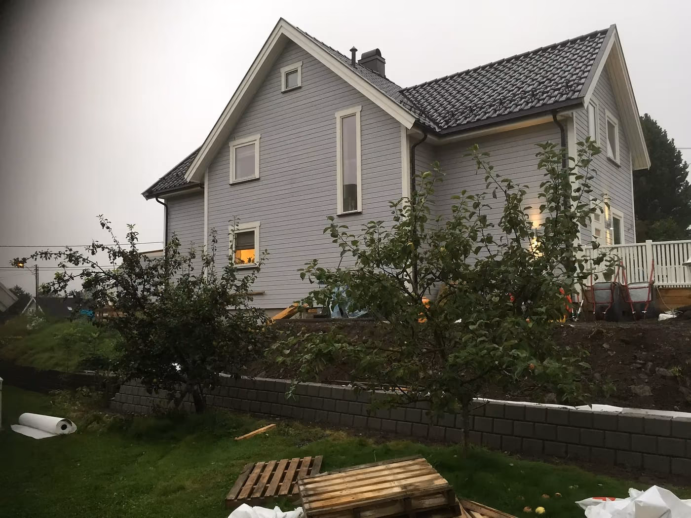 Grå enebolig med nytt tak, sett fra hagen med nystøpt støttemur i betongblokk.