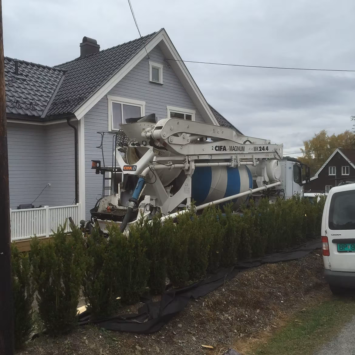 Betongbil med pumpekran plassert ved enebolig under grunnarbeid.
