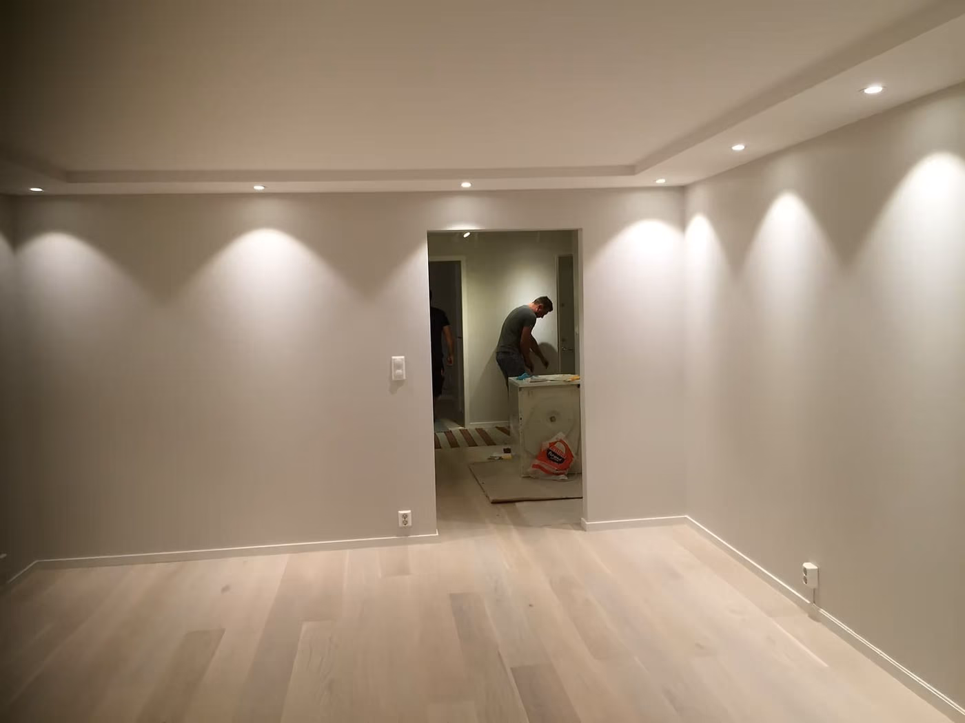 Nyoppusset stue med downlights, lys parkett og håndverker i døråpningen bak.