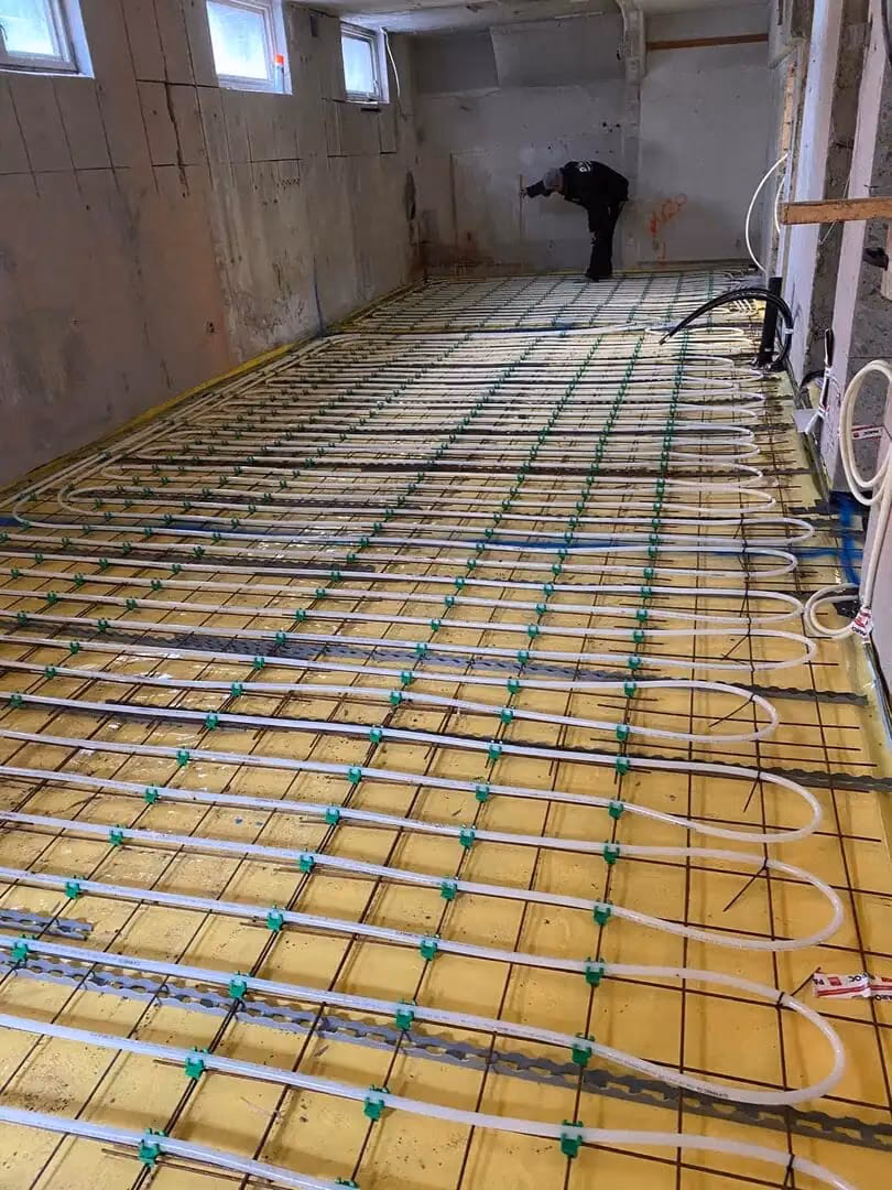 Installasjon av varmesystem med gulvvarme og rør i nybygg, med en person som jobber i bakgrunnen. Perfekt for oppvarming og energieffektivitet.