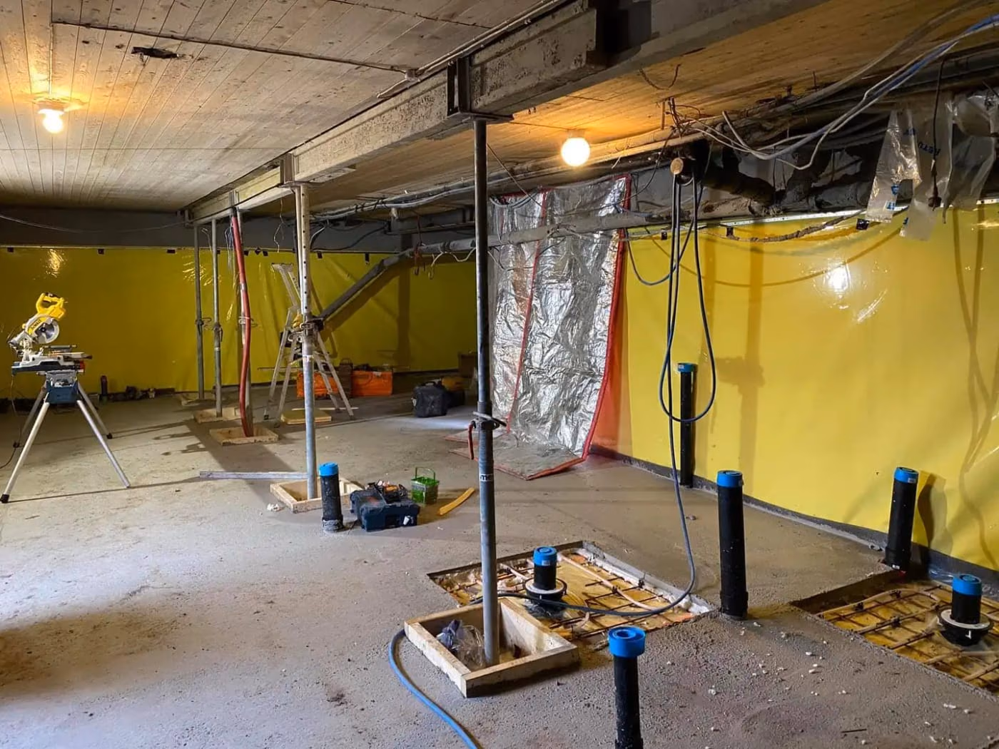 Innendørs byggeplass med støttestrukturer, verktøy og utstyr for bygg- og gravearbeid, klar for videre konstruksjon og utendørs arbeid.