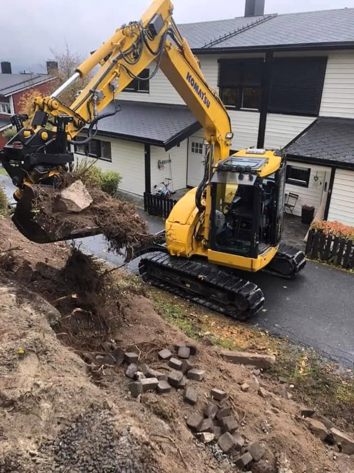 Minigraver i arbeid for jord- og grunnarbeid i boligområde, med fokus på profesjonell bygg- og gravearbeid, utendørs, maskinpark, anlegg, og tomteforberedelser.