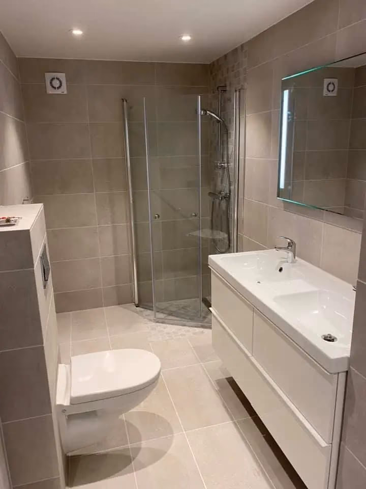 Bilde av et moderne bad med dusjhjørne, vegg- og gulvfliser i nøytrale toner, og et hvitt vaskeskap med speil. Perfekt for oppussing og renovering av bad.