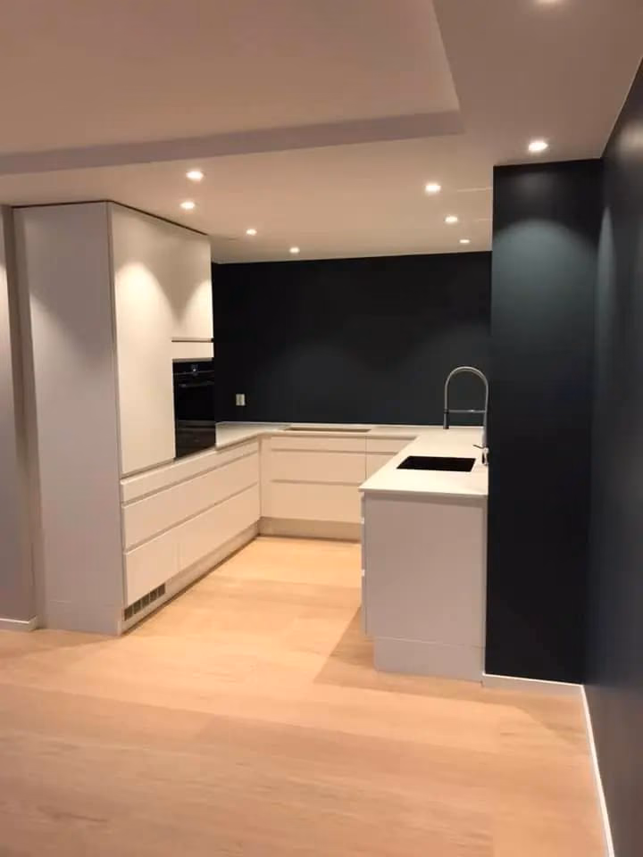 Moderne kjøkken med hvite skap, svart vegg og integrert oppvaskkum, perfekt for moderne hjem. Kjøkkenet har minimalistisk design og god oppbevaringsplass.