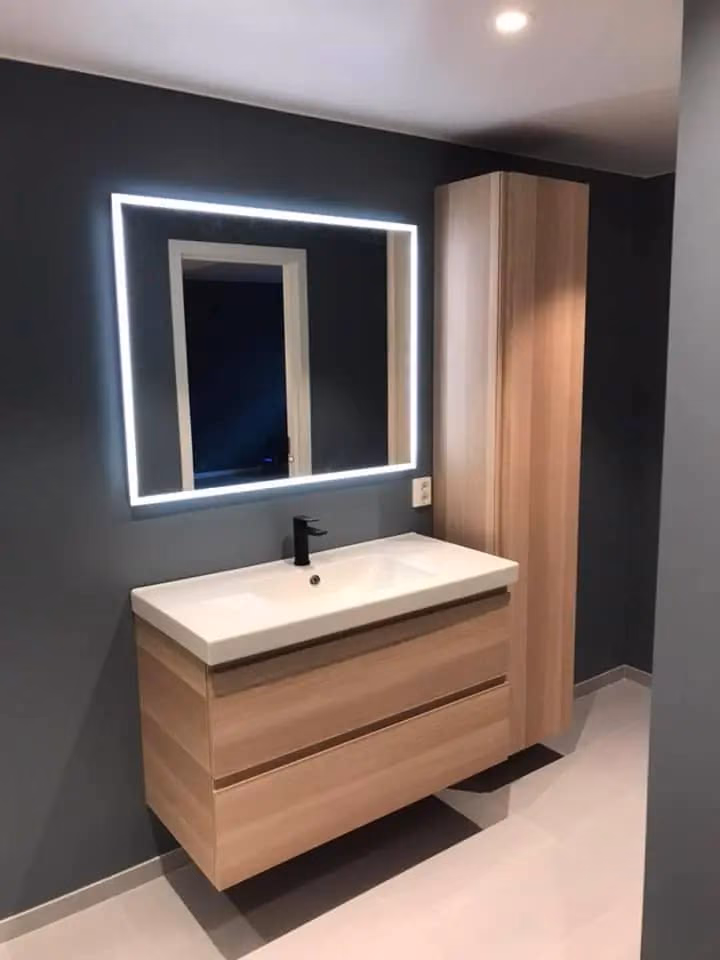 Elegant bad med veggmontert speil med LED-lys, moderne servant og oppbevaringsskap i lyst treverk, perfekt for oppussing og badrenovering.
