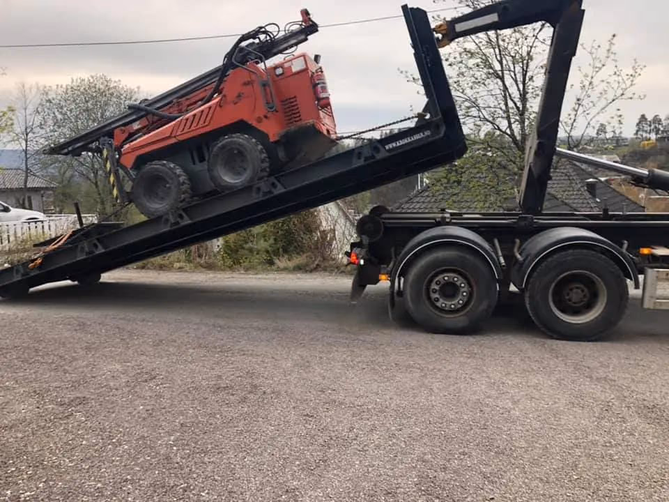 Minigraver på tilhenger for transport, klar for gravearbeid i Bærum. Profesjonell bygg- og grave service med pålitelig maskintransport og anleggstjenester.
