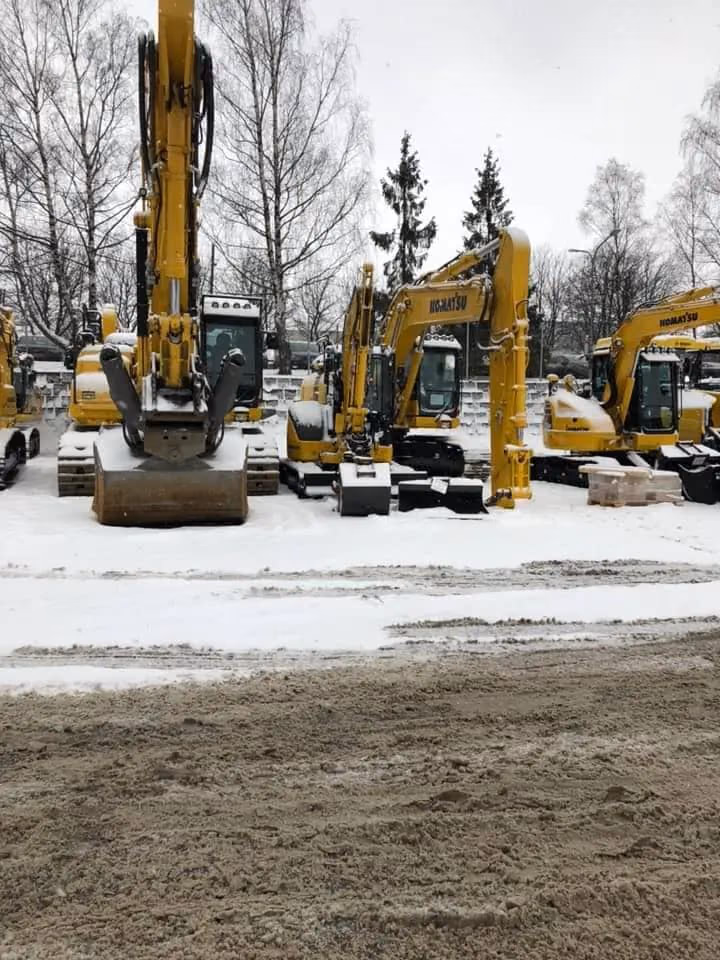 Flere gravemaskiner i Bærum, klare for grave- og byggarbeid, med snødekke og vinterlandskap i bakgrunnen. Perfekt for anlegg og graveprosjekter.